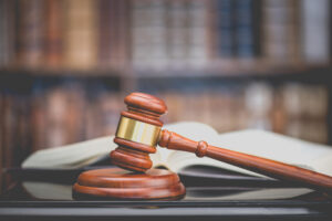 Legal office of lawyers, justice and law concept : Judge's gavel or hammer and base used by a judge person on a desk in a courtroom with blurred books and a bookshelf or bookcase in the background.